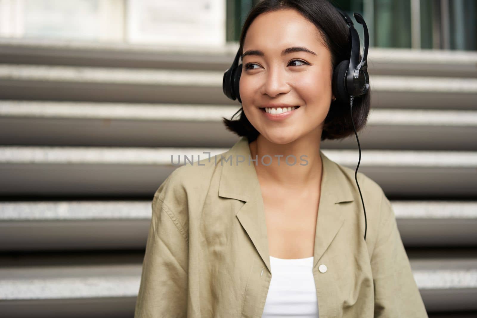 Portrait of beautiful girl in earphones, listening music, smiling and walking in city centre.
