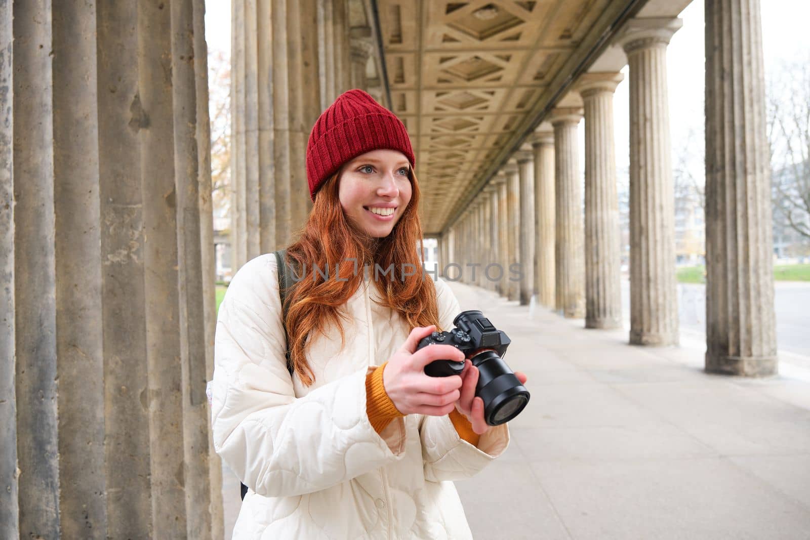 Smiling tourist photographer, takes picture during her trip, holds professional camera and makes photos by Benzoix
