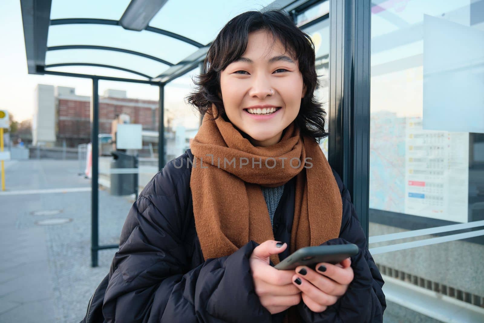 Beautiful young woman, standing on bus stop, waiting for her public transport, using mobile phone, using smartphone application by Benzoix