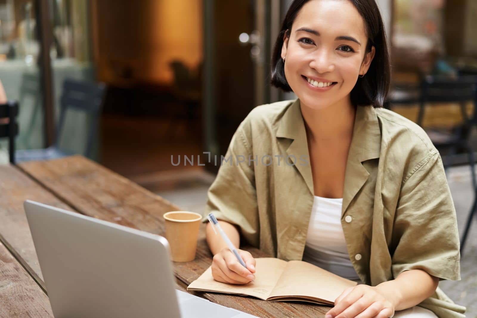 Portrait of young korean girl making notes, listening online meeting, lecture, looking at laptop screen, working remotely from cafe by Benzoix