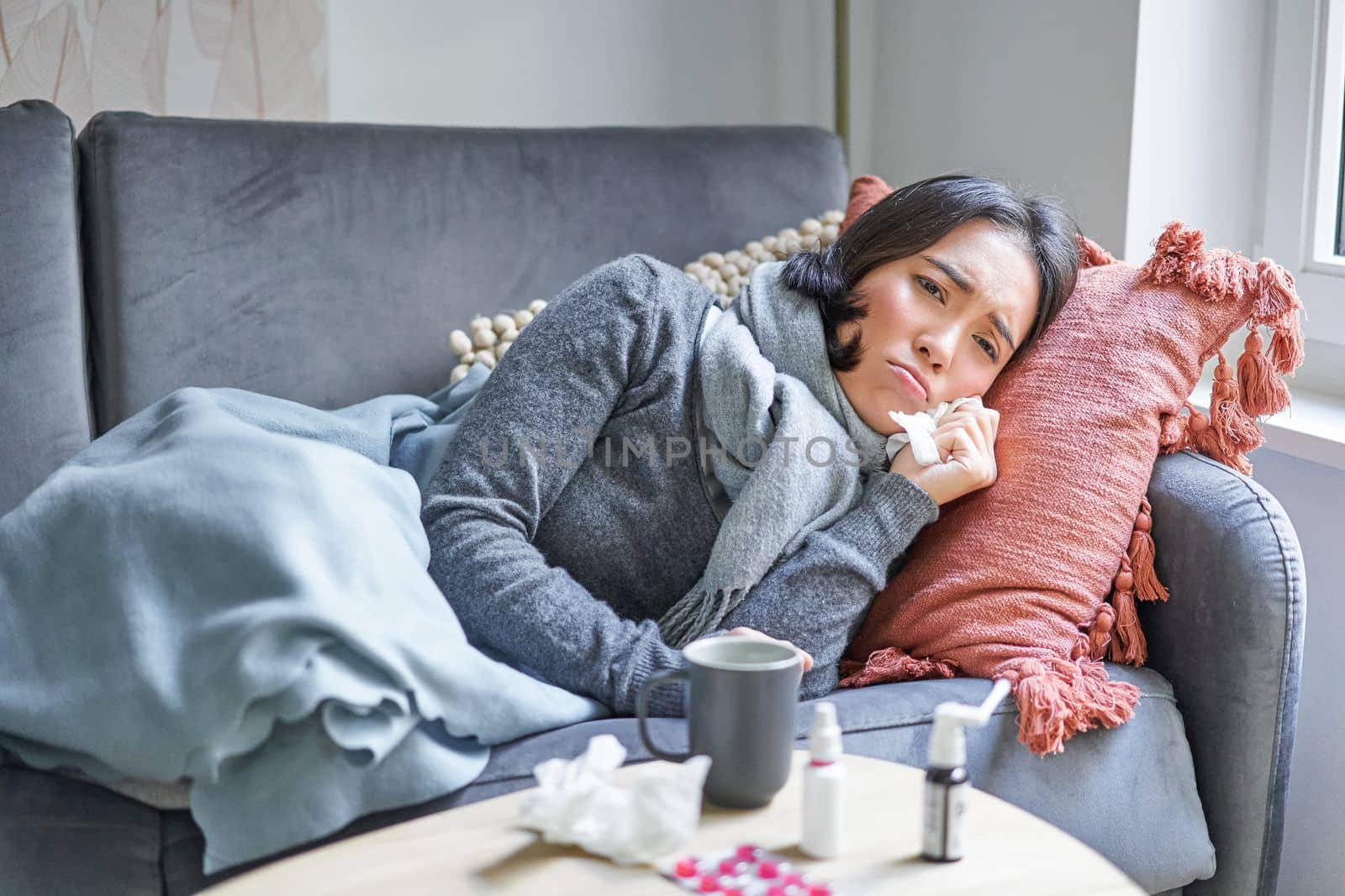 Sick woman lying on sofa at home, catching cold. Young girl freezing from heating problem in her apartment, concept of high cost of living.