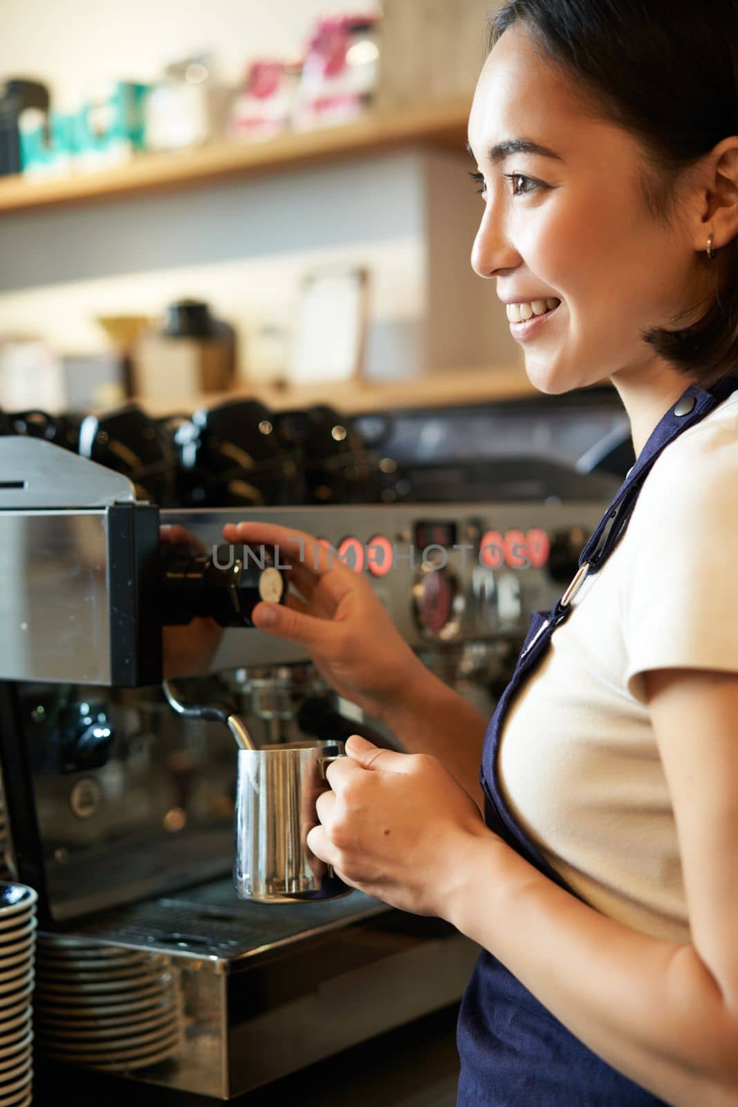Happy asian woman, barista using coffee machine to make order, steaming milk for cappuccino and latte, laughing and smiling while working in cafe by Benzoix