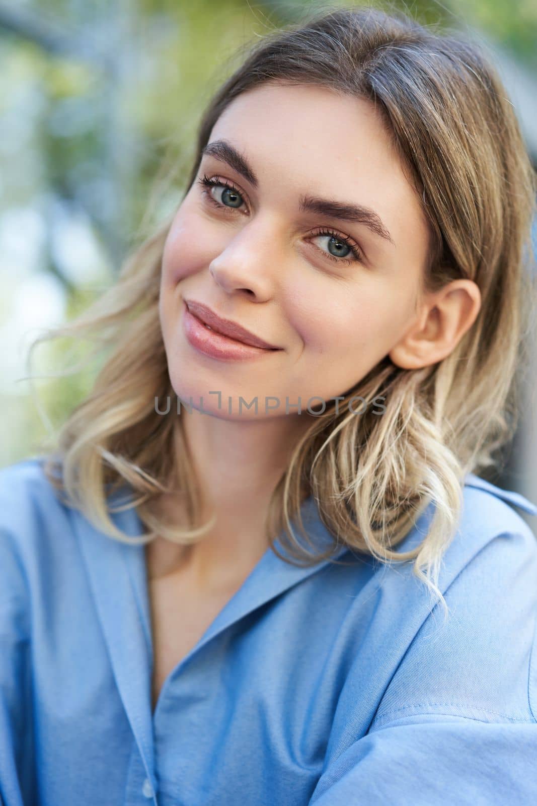 Vertical portrait of beautiful adult woman, sitting in blue collar shirt outdoors, smiling and looking cute at camera by Benzoix