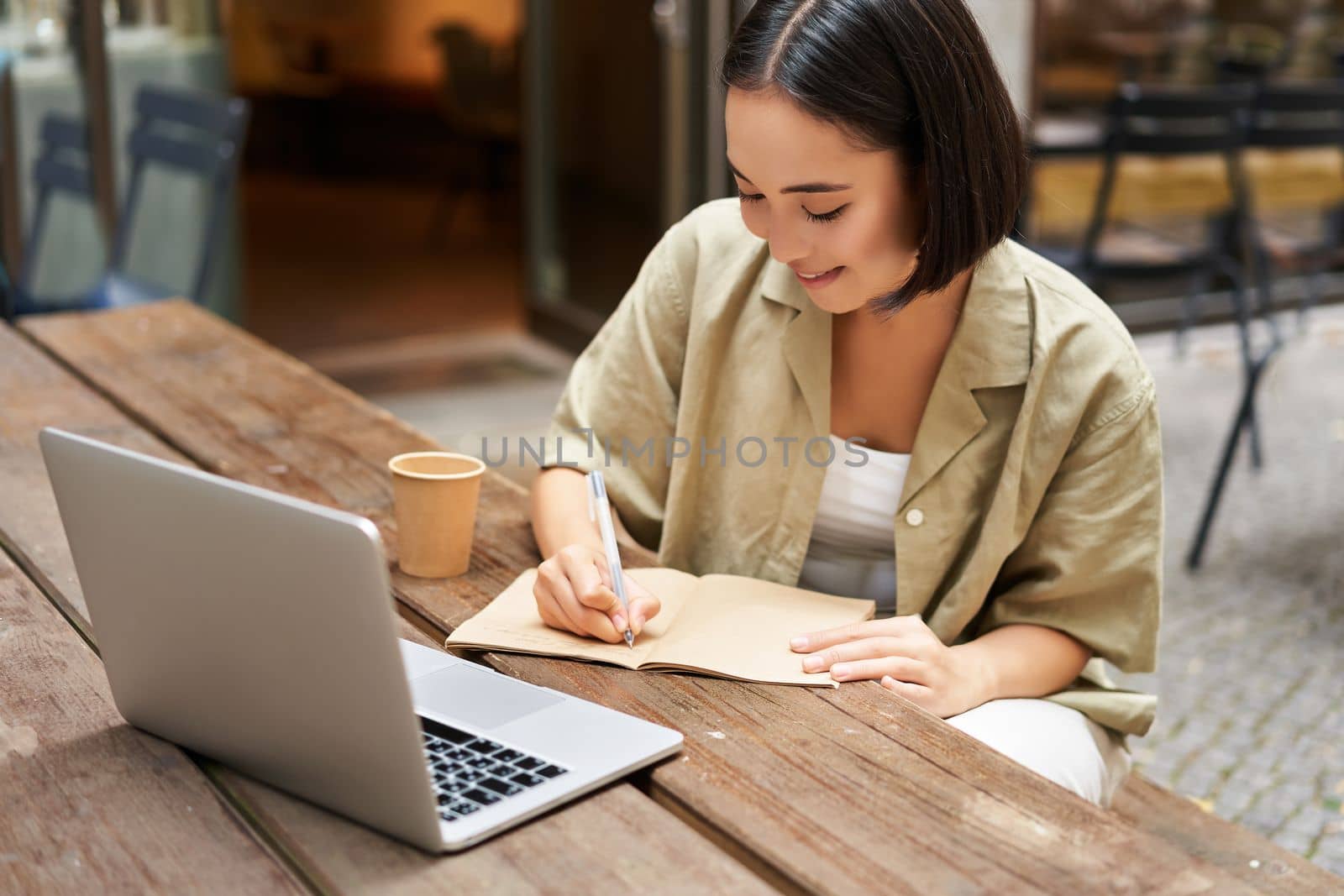 Portrait of young asian woman working on laptop, making notes, writing down while attending online lesson, work meeting.