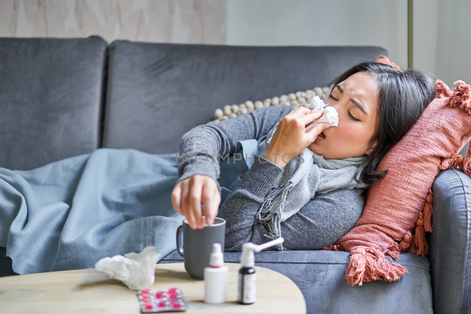 Sick woman lying on sofa at home, catching cold. Young girl freezing from heating problem in her apartment, concept of high cost of living.