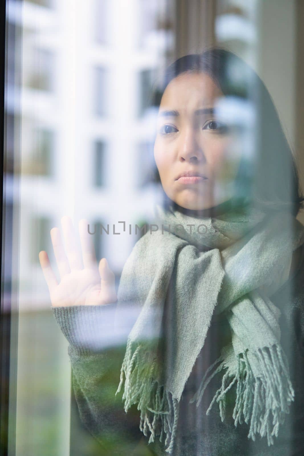 Asian woman feels unwell, stays at home, looks outside window with jealous, distressed face, wants go outside but caught cold.