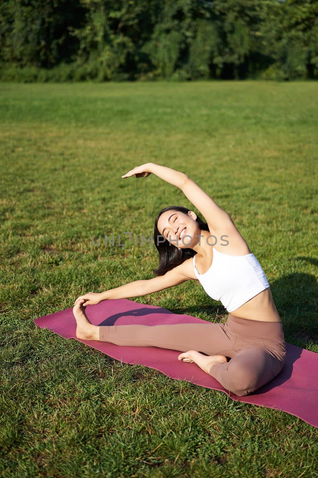 Young woman does yoga on lawn in park, stretching on fitness mat, wellbeing concept by Benzoix