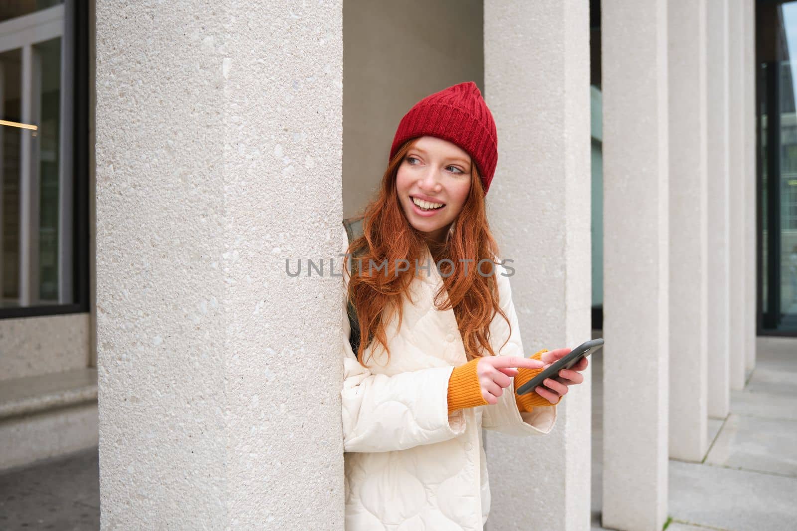 Stylish urban girl using mobile phone app, standing in city, waiting for taxi, looking at smartphone application, texting message.