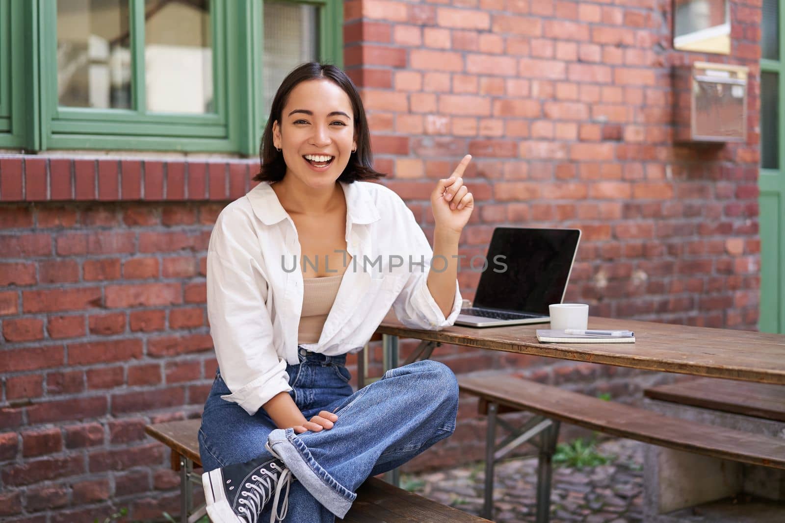 Enthusiastic asian woman, pointing at upper right corner, showing advertisement, news on banner, looking impressed and intrigued by smth.