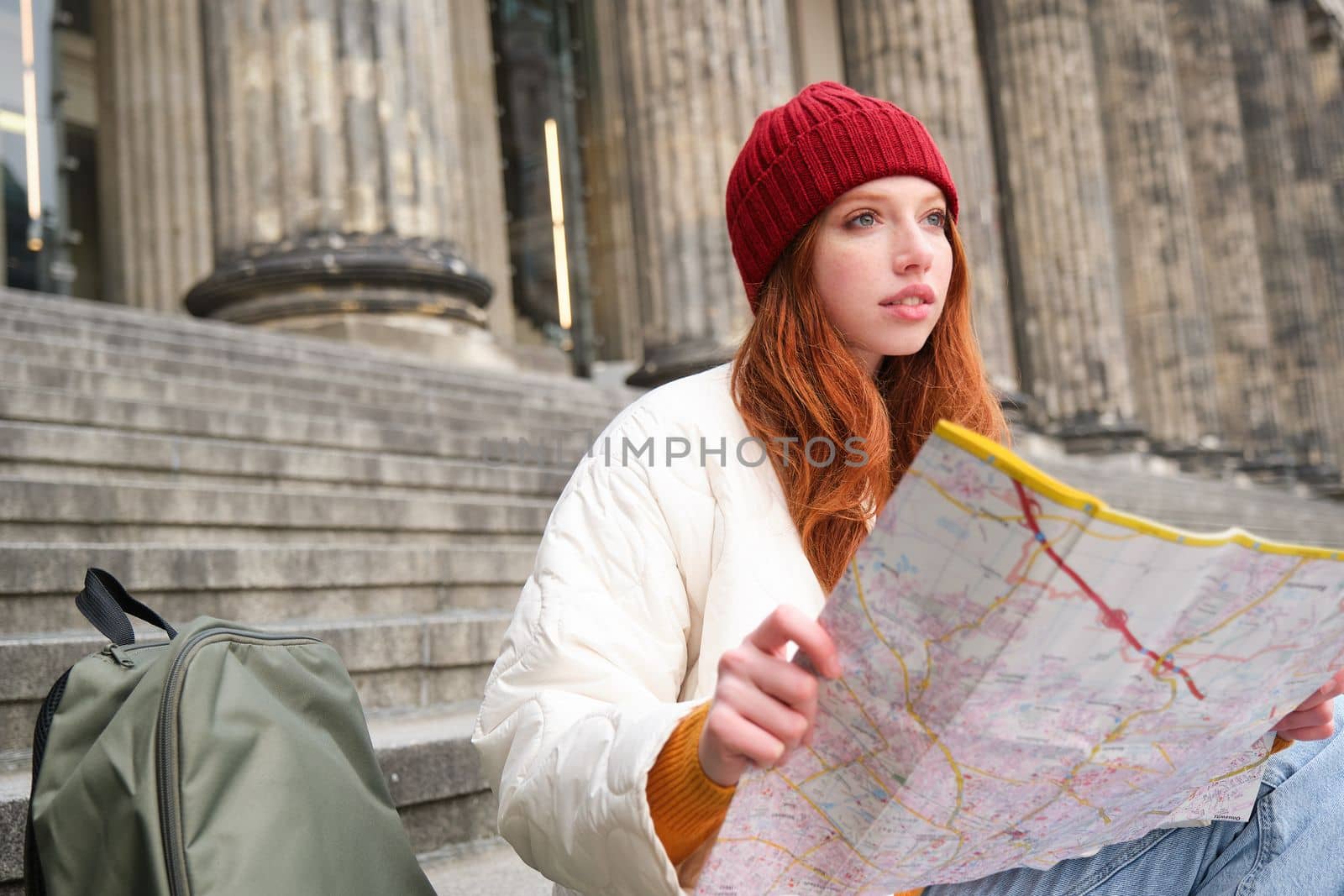 Beautiful young woman, traveler with backpack holds paper map, explores city sightseeing, plans route for tourism popular attractions by Benzoix