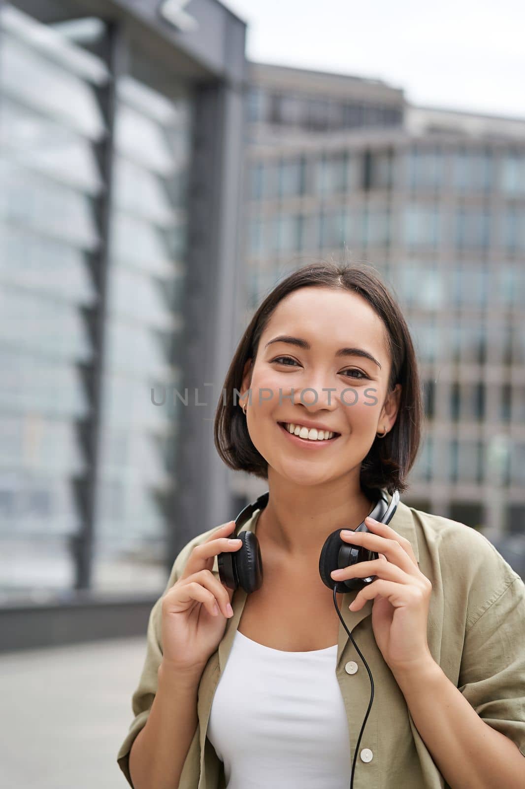 People. Portrait of smiling asian girl with headphones, dancing on street of city centre, looking happy.