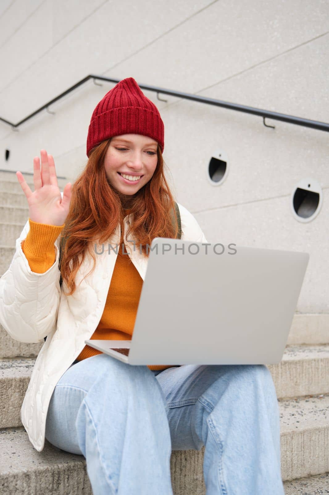 Portrait of happy young woman, redhead girl with laptop, waves hand and says hello on video chat, has conversation on computer application, talks to someone.