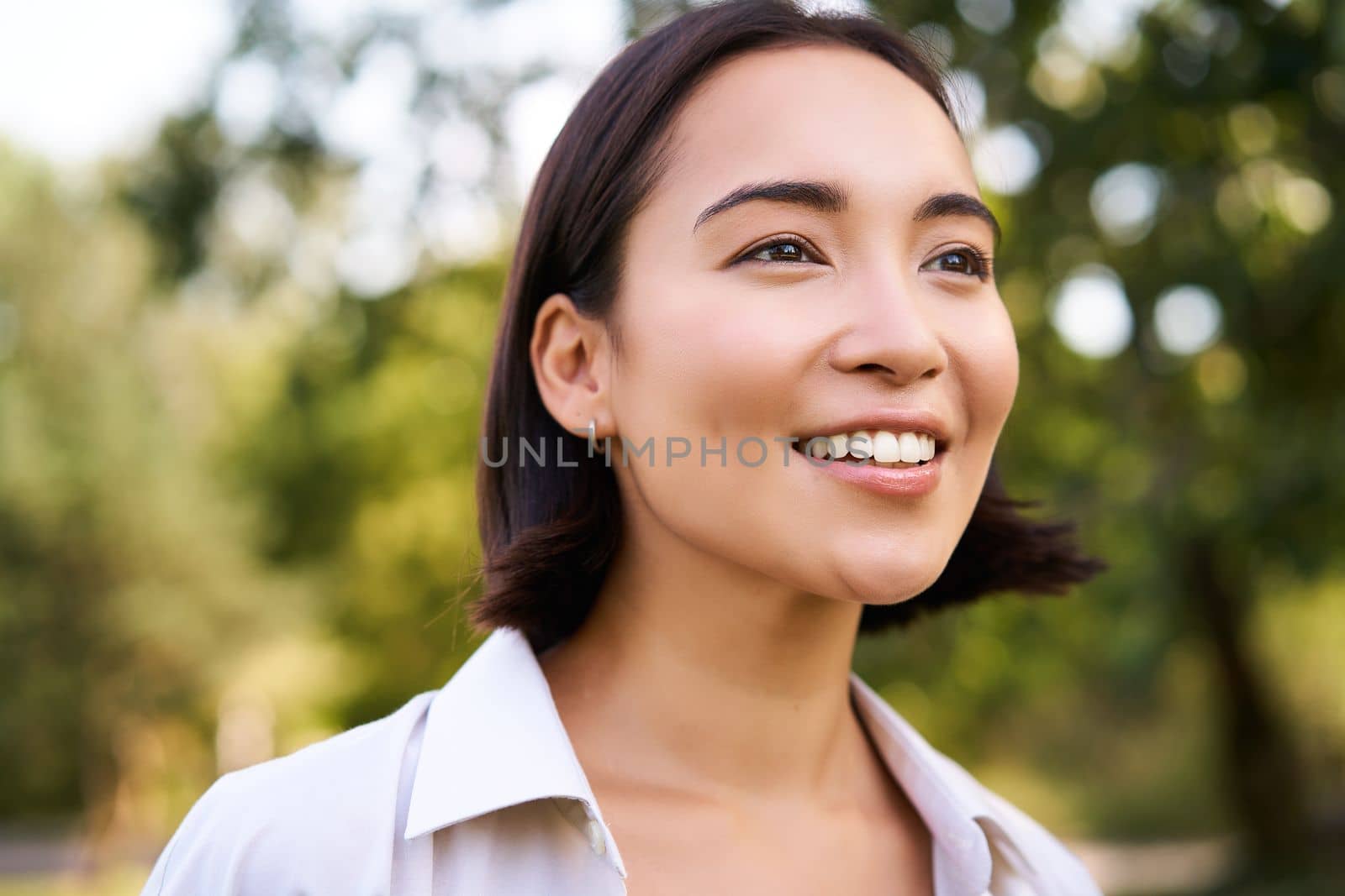 Close up face of asian happy girl, smiling and looking at camera carefree, walking in park by Benzoix