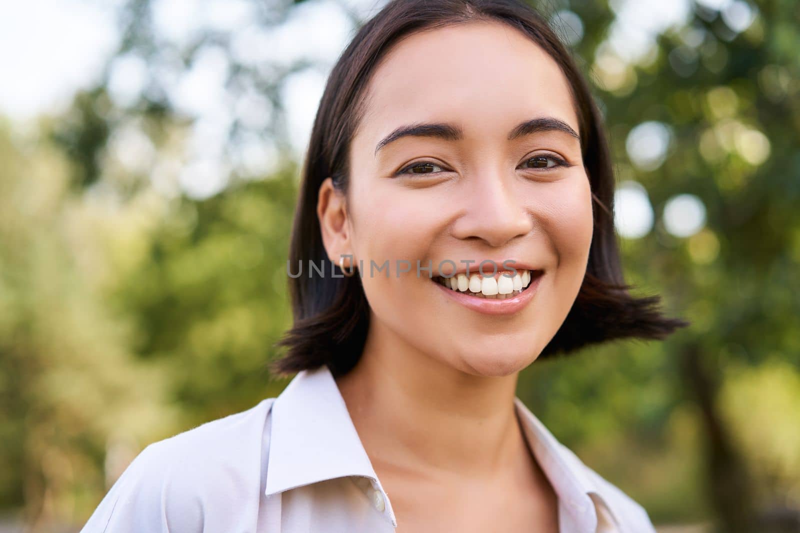 Close up face of asian happy girl, smiling and looking at camera carefree, walking in park by Benzoix