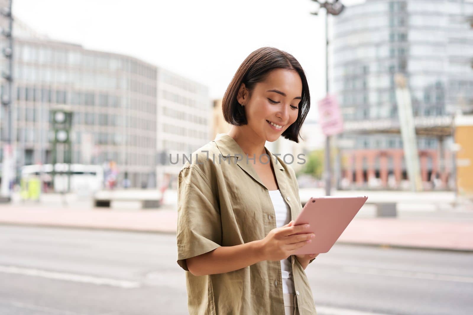 Portrait of young stylish woman walking with tablet, going somewhere in city by Benzoix