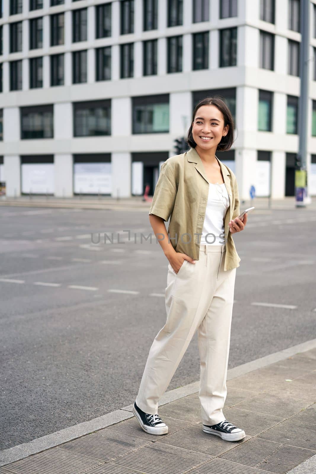 Woman smiling, standing with smartphone on street, waiting for taxi, checking mobile phone app by Benzoix