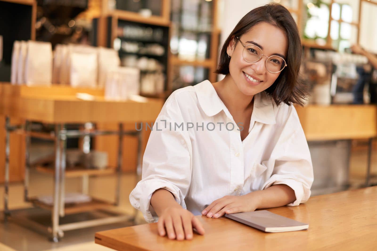 Portrait of young stylish businesswoman in cafe, sitting with notebook, making notes, working at coworking space.