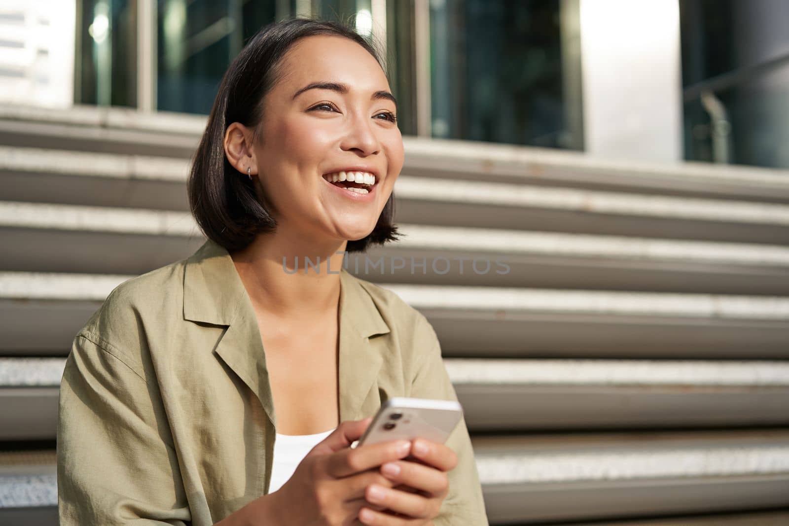 Beautiful asian girl sits on stairs with smartphone. Young korean woman resting outdoors, using mobile phone application by Benzoix