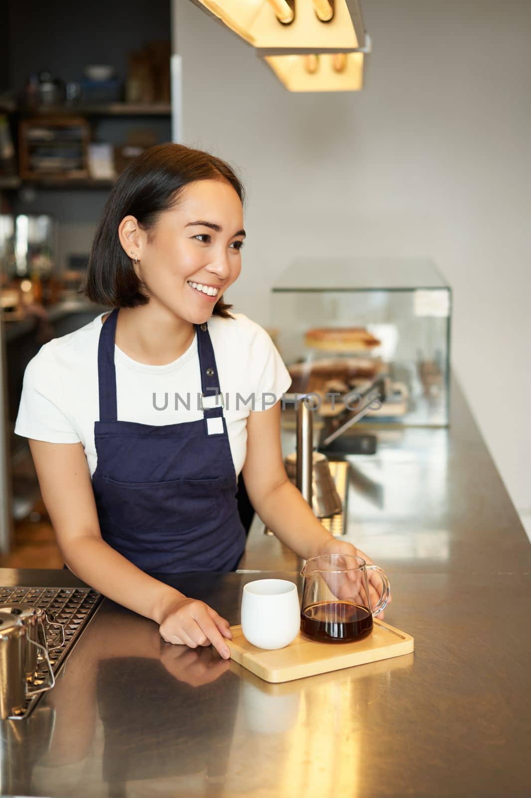 Vertical shot of smiling asian barista, girl working in cafe, giving order to client, made batch brew, filter coffee by Benzoix