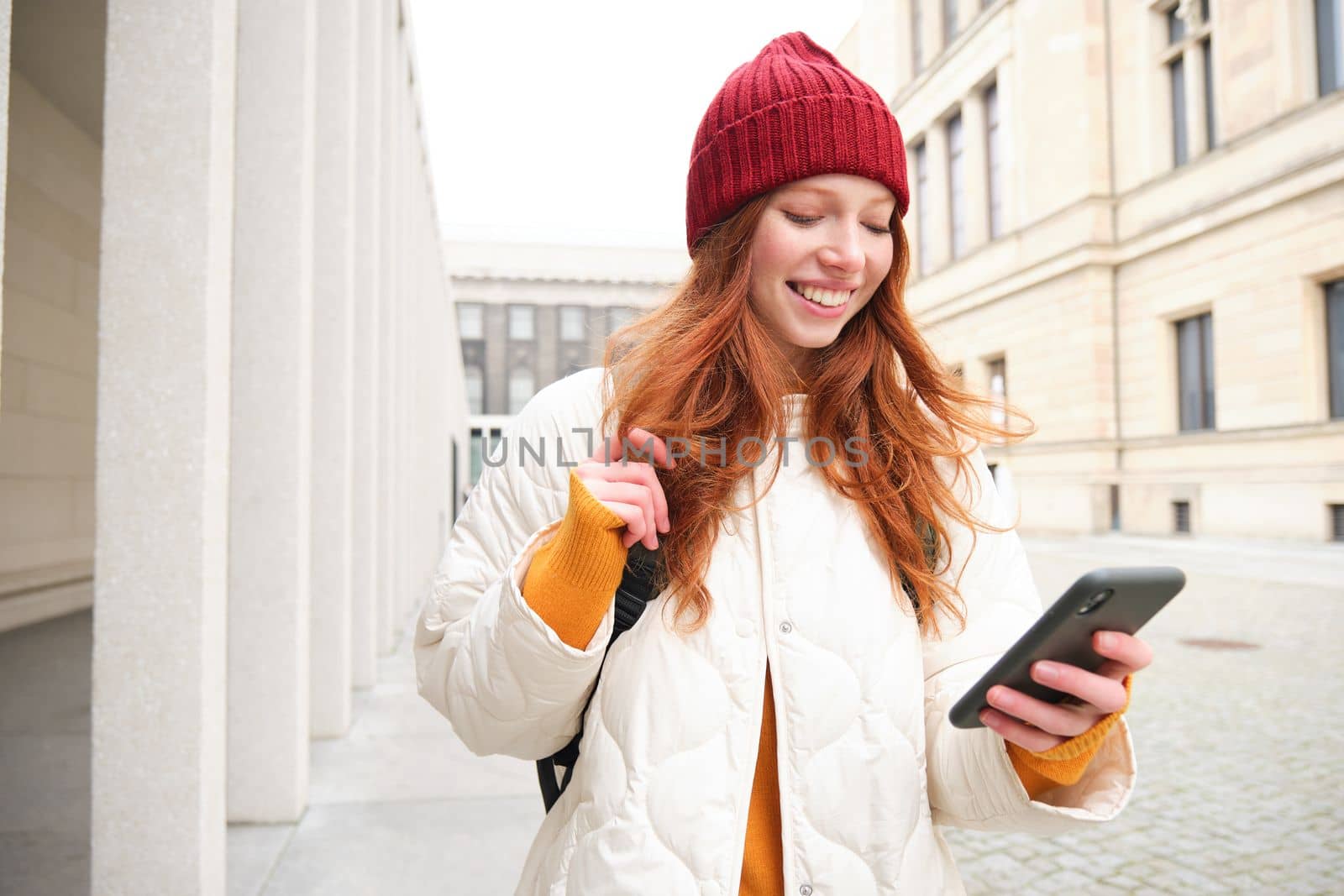 Beautiful smiling girl, tourist with backpack, holding smartphone, using map on mobile phone application, looking for sightseeing in internet app, standing outdoors by Benzoix