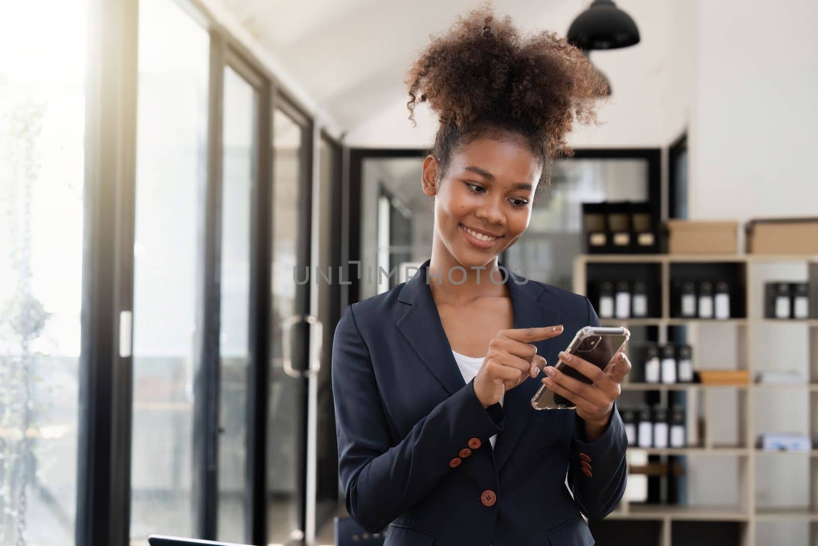 Image of young woman holding cellphone while working in office.