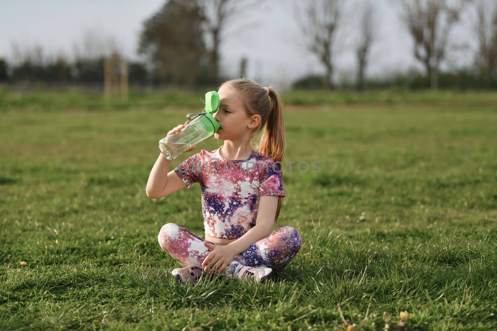 A girl drinking water at the stadium by Godi