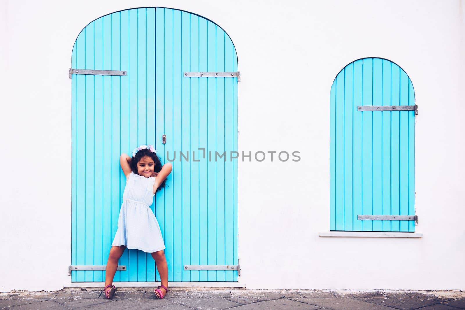 funny little girl making fun, she is in front of a white wall with a door and a turquoise wooden window