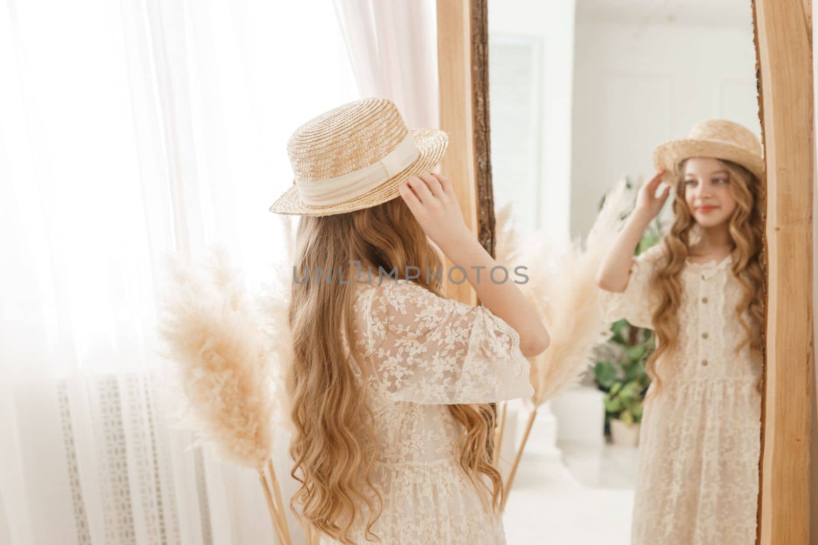 A beautiful teenage girl with long hair measures a straw hat in front of a mirror. Self-admiration of a blonde. selective focus