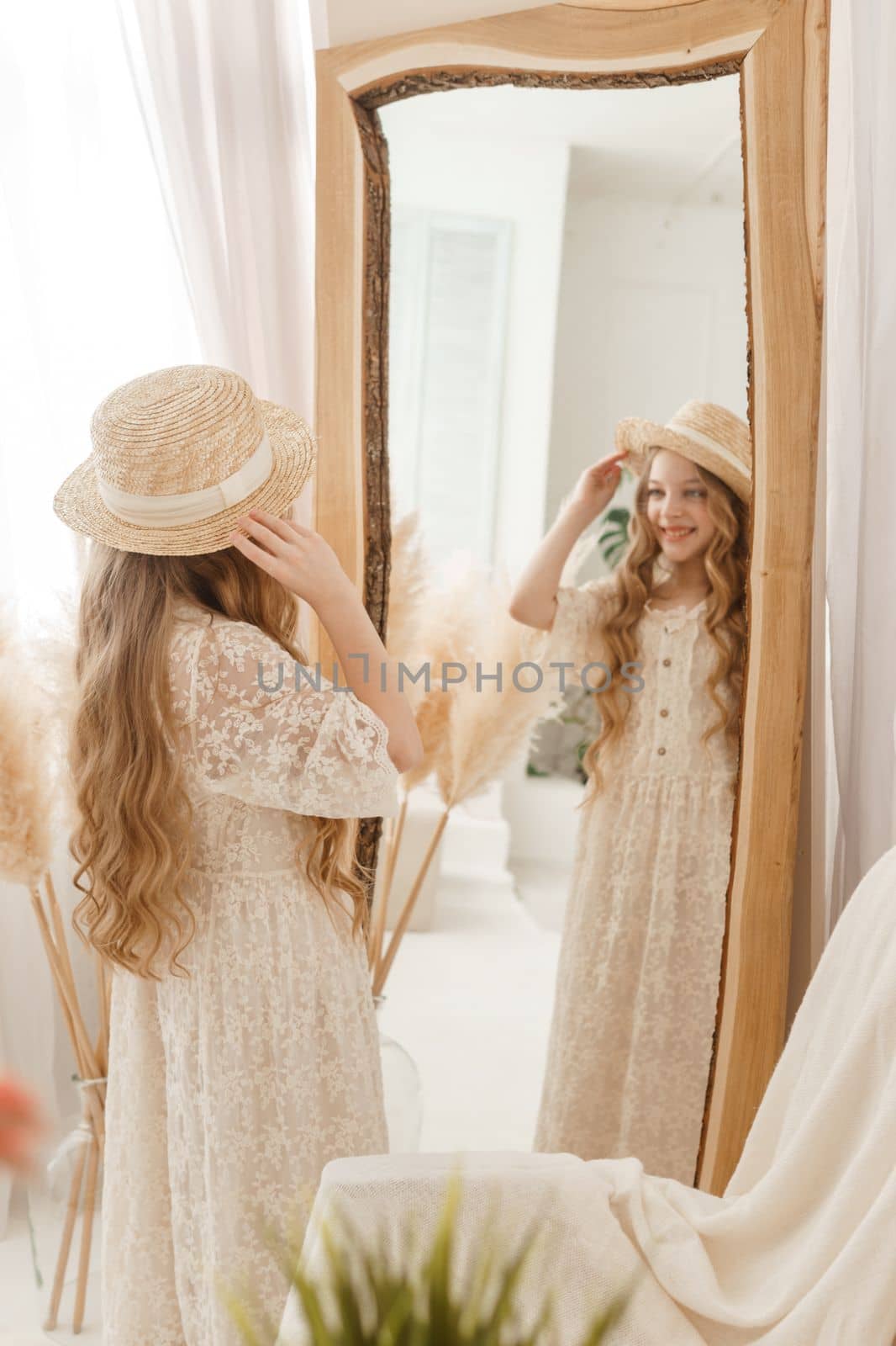 A beautiful teenage girl with long hair measures a straw hat in front of a mirror. Self-admiration of a blonde. selective focus