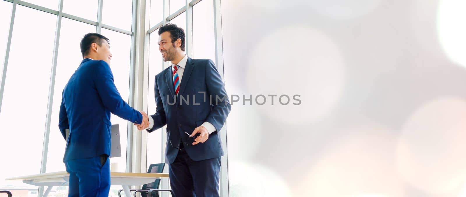 Business people handshake in corporate office in widen view showing professional agreement on a financial deal contract.