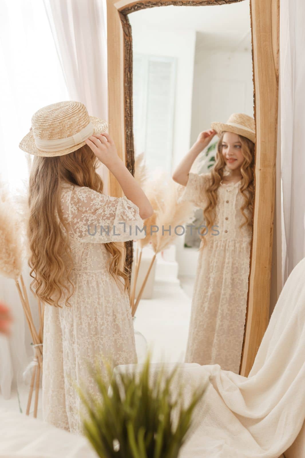 A beautiful teenage girl with long hair measures a straw hat in front of a mirror. Self-admiration of a blonde. selective focus