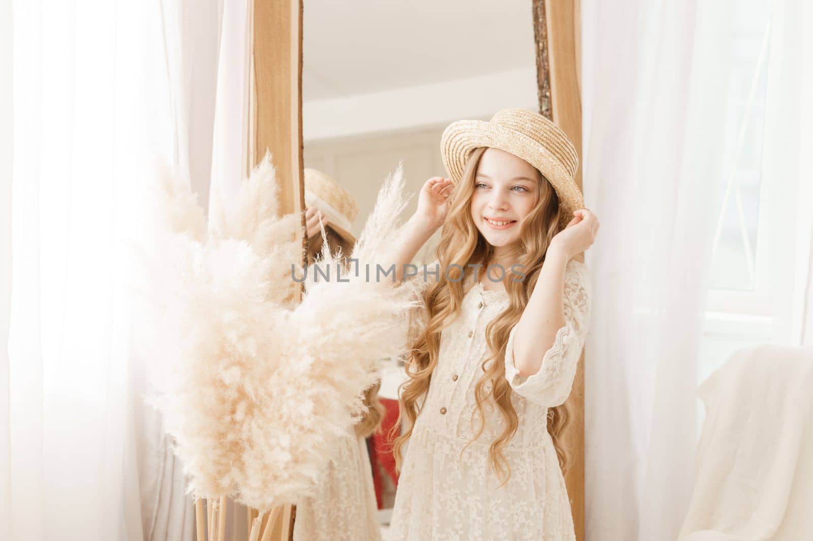 A beautiful teenage girl with long hair measures a straw hat in front of a mirror. Self-admiration of a blonde. selective focus