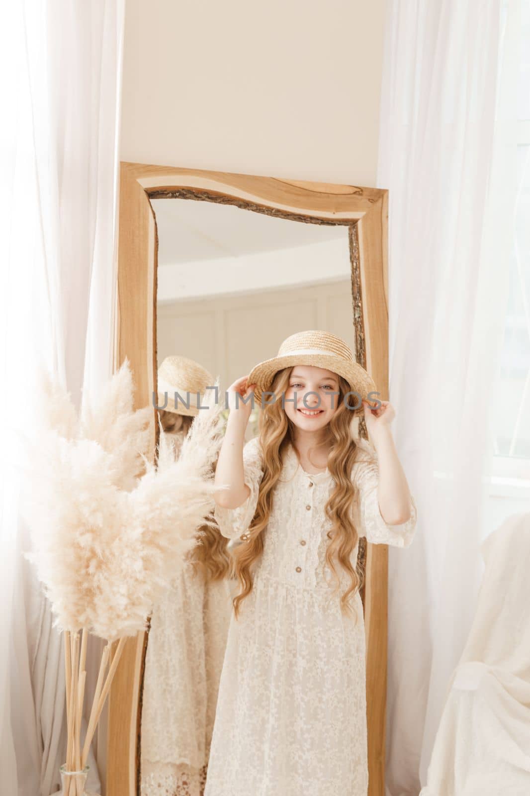 A beautiful teenage girl with long hair measures a straw hat in front of a mirror. Self-admiration of a blonde. selective focus