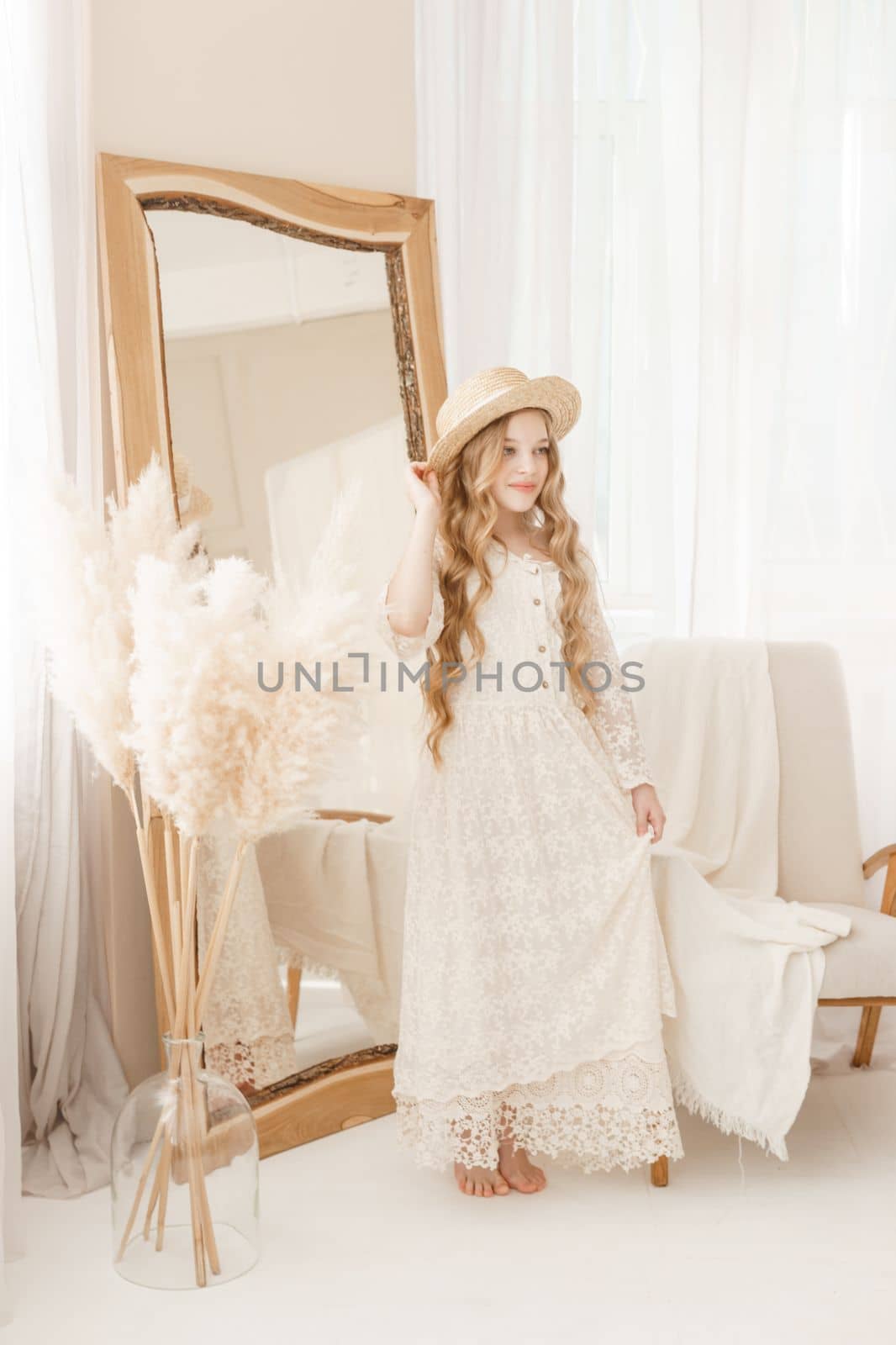 A beautiful teenage girl with long hair measures a straw hat in front of a mirror. Self-admiration of a blonde. selective focus