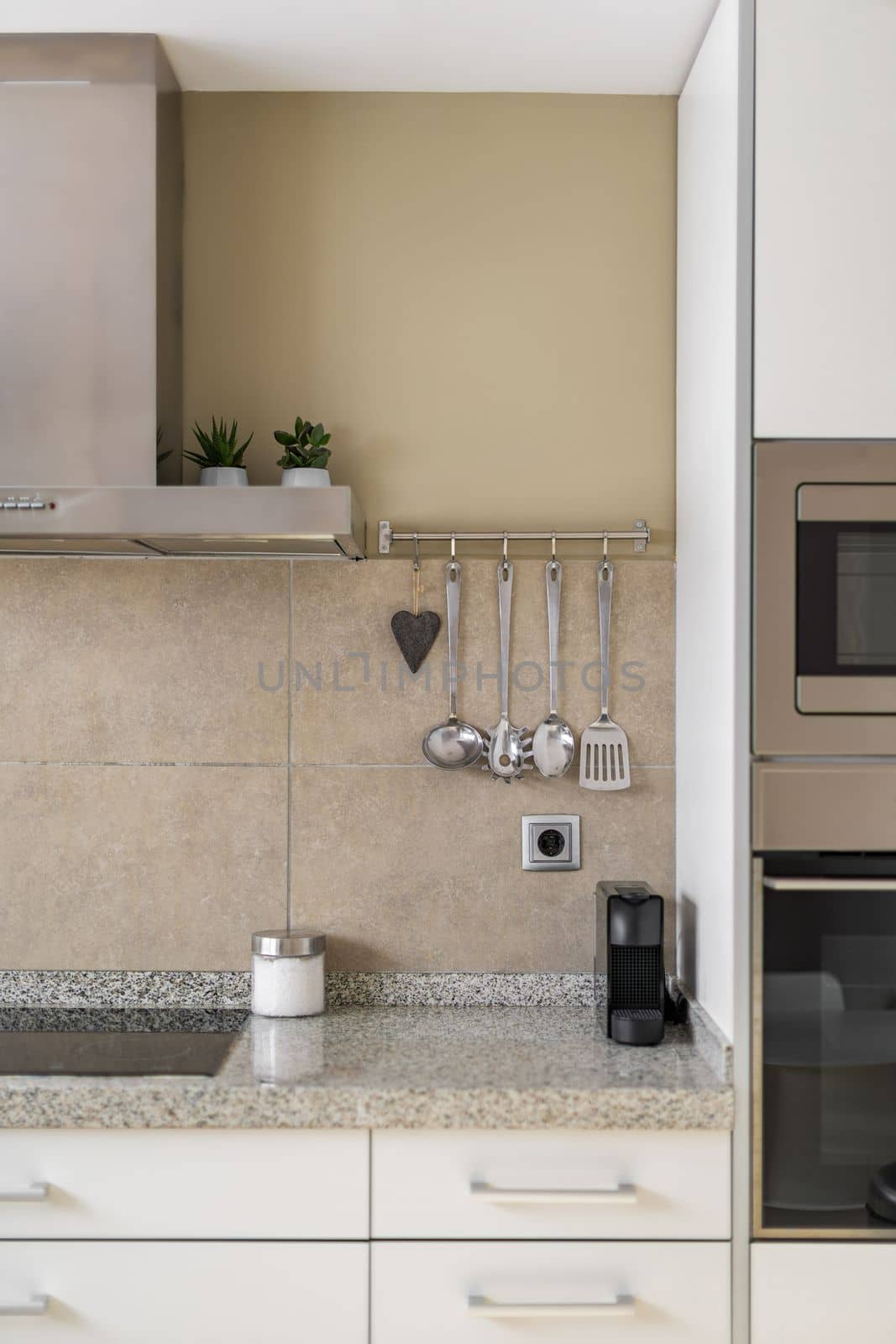 Part of kitchen with marble countertop, wall with beige marble tiles. Kitchen is equipped with new electronic appliances and utensils for convenience and preparation of delicious meals