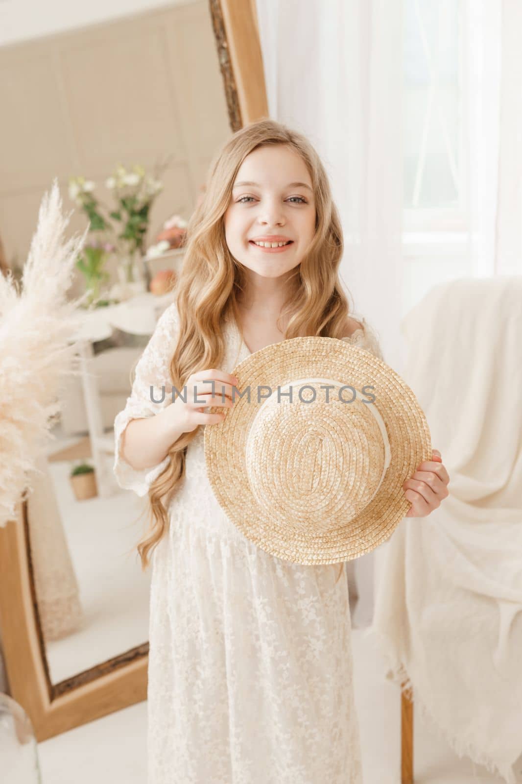 A beautiful teenage girl with long hair measures a straw hat in front of a mirror. Self-admiration of a blonde. selective focus