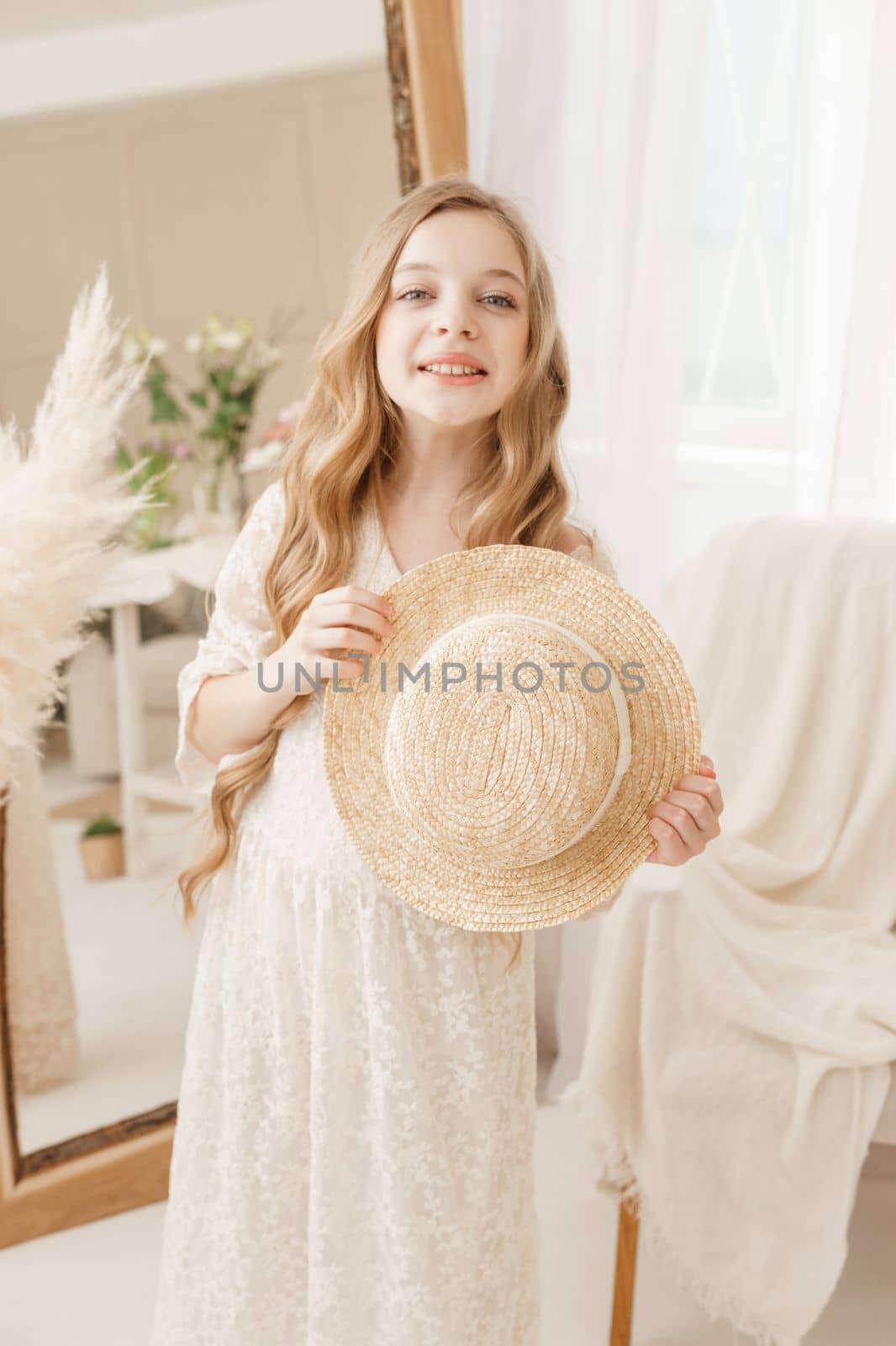 A beautiful teenage girl with long hair measures a straw hat in front of a mirror. Self-admiration of a blonde. selective focus