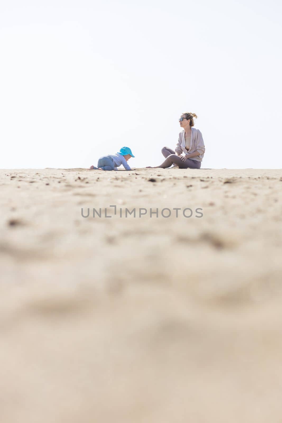 Mother playing his infant baby boy son on sandy beach enjoying summer vacationson on Lanzarote island, Spain. Family travel and vacations concept. Copy space.