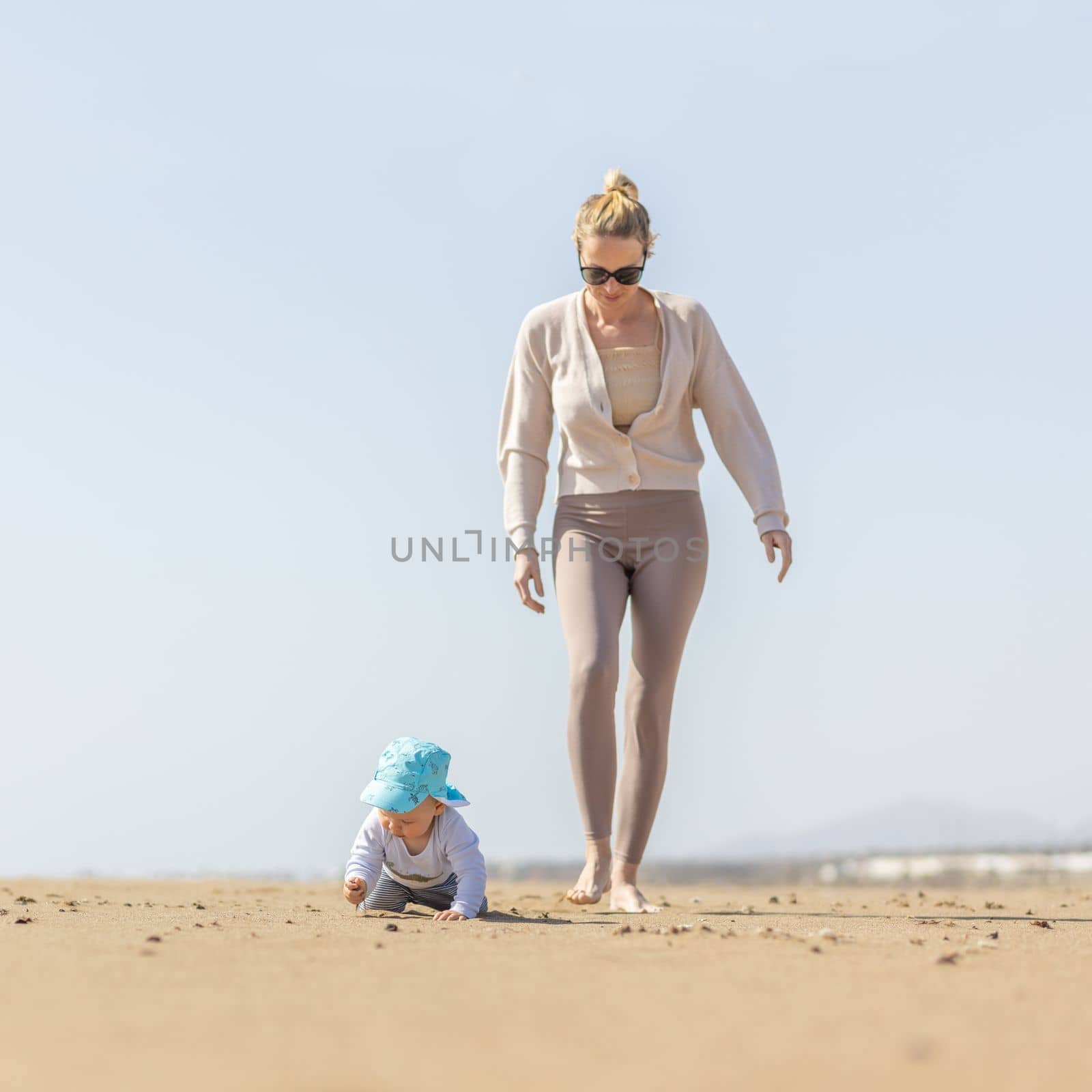 Mother playing his infant baby boy son on sandy beach enjoying summer vacationson on Lanzarote island, Spain. Family travel and vacations concept. by kasto