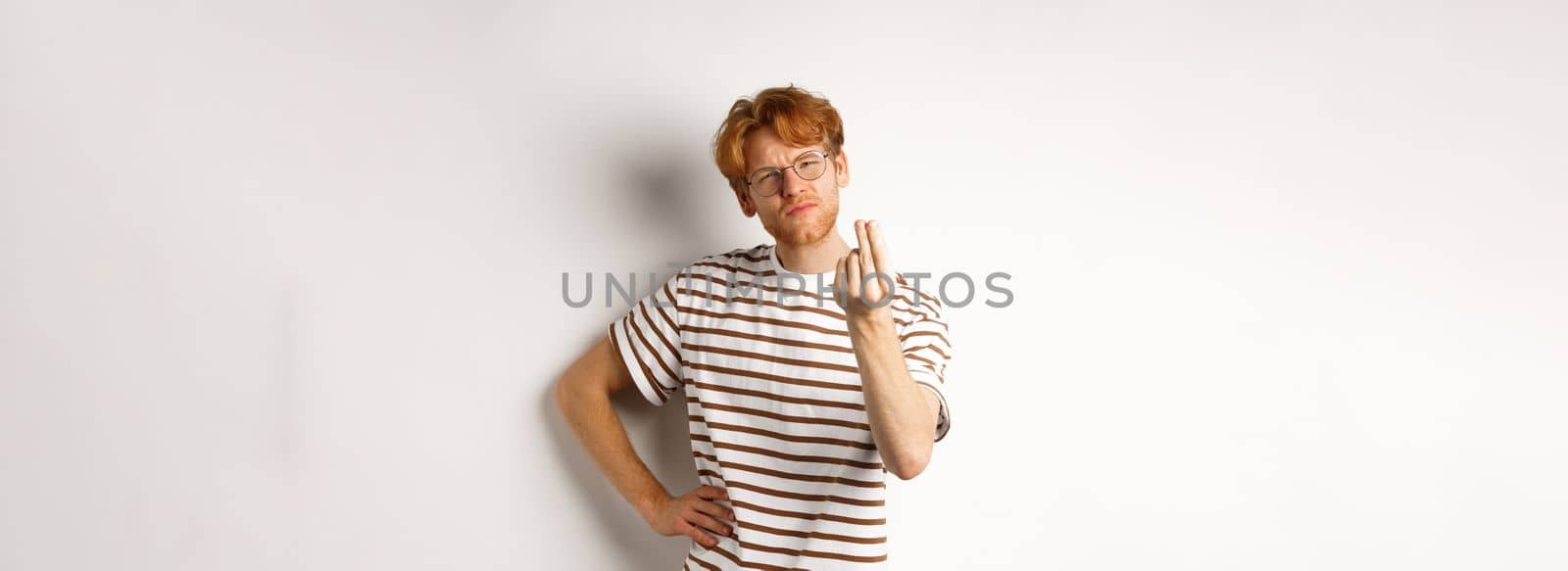 Image of satisfied young man with red hair and glasses showing chefs kiss gesture to praise something perfect, standing over white background.