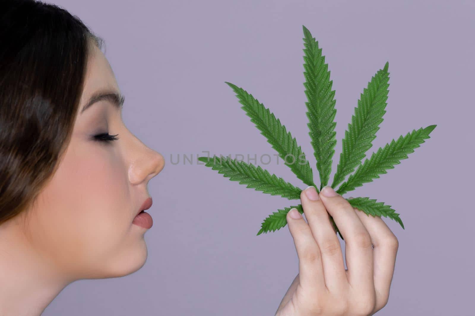 Closeup charming girl with fresh skin hold green leaf for beauty skin care made from cannabis leaf. Cosmetology and cannabis concept with isolated background. Woman holding cbd leaf side view.