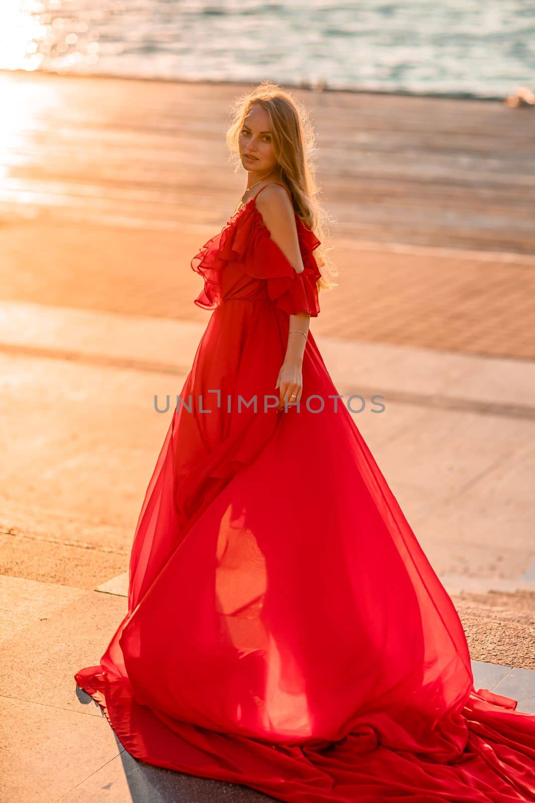 Sunrise red dress. A woman in a long red dress against the backdrop of sunrise, bright golden light of the sun's rays. The concept of femininity, harmony