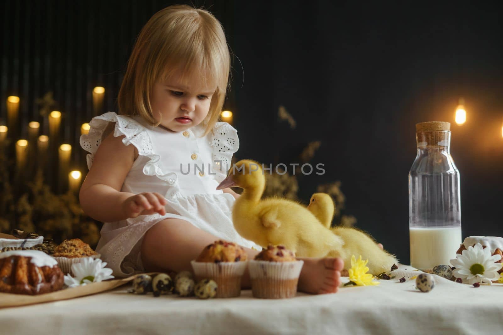 A little girl is sitting on the Easter table and playing with cute fluffy ducklings. The concept of celebrating happy Easter