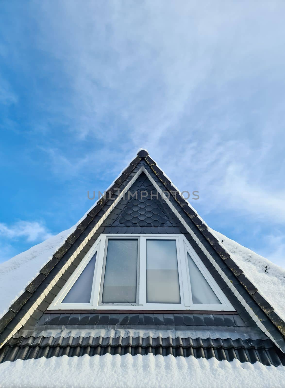 Open roof window in velux style with black roof tiles covered in snow