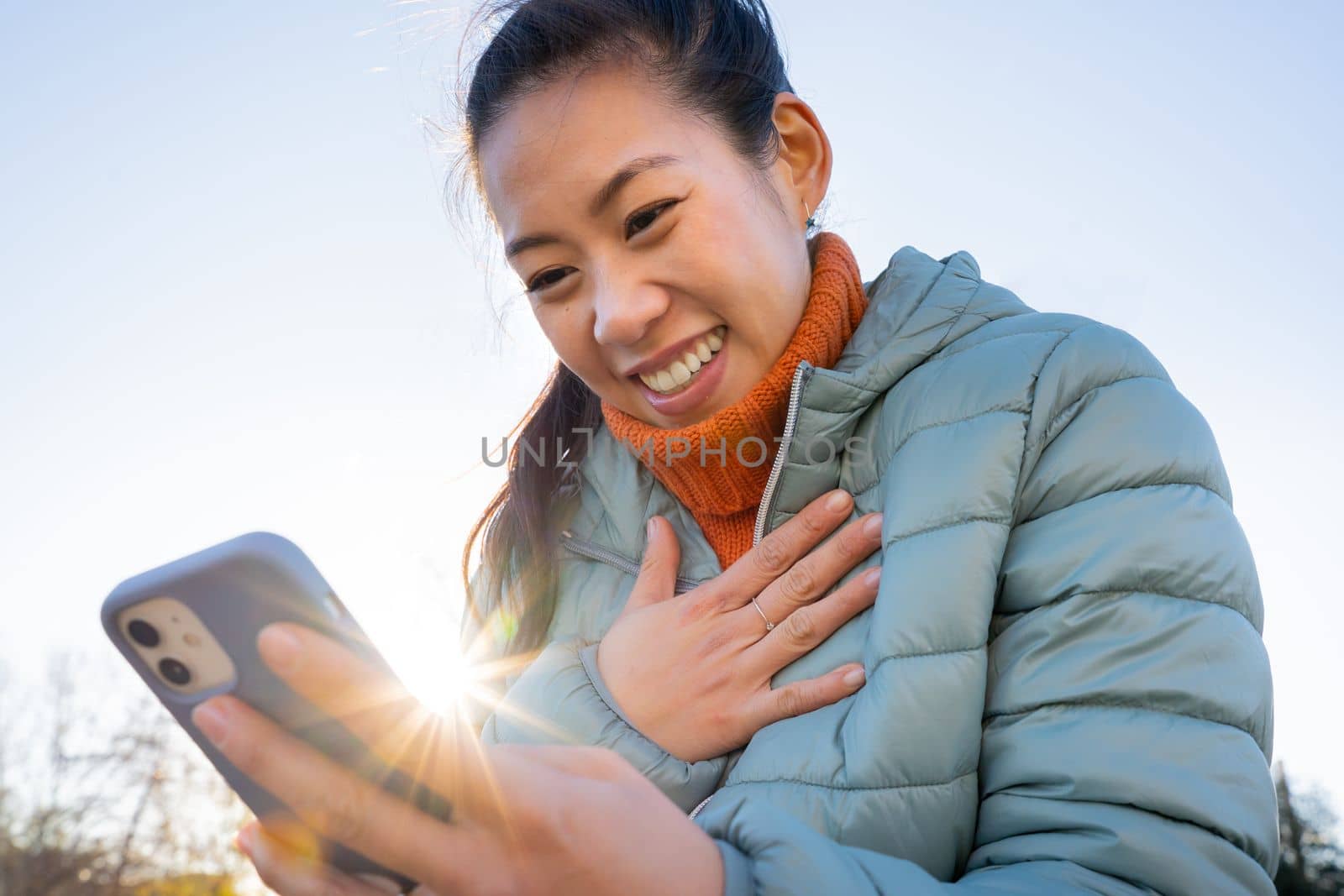 Attractive Asian Chinese woman happy smiling and laughing looking at smart phone outdoors. Real beautiful people and technology concept.