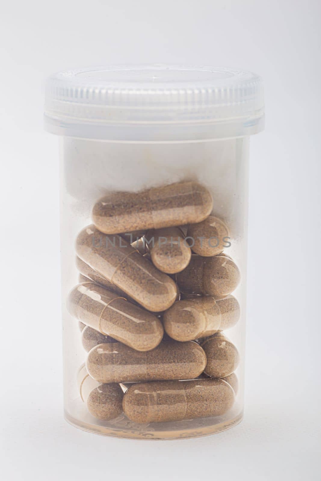 Transparent pill, fill with brown natural ingredient, in a closed tranparent bottle with cotton ball topper
