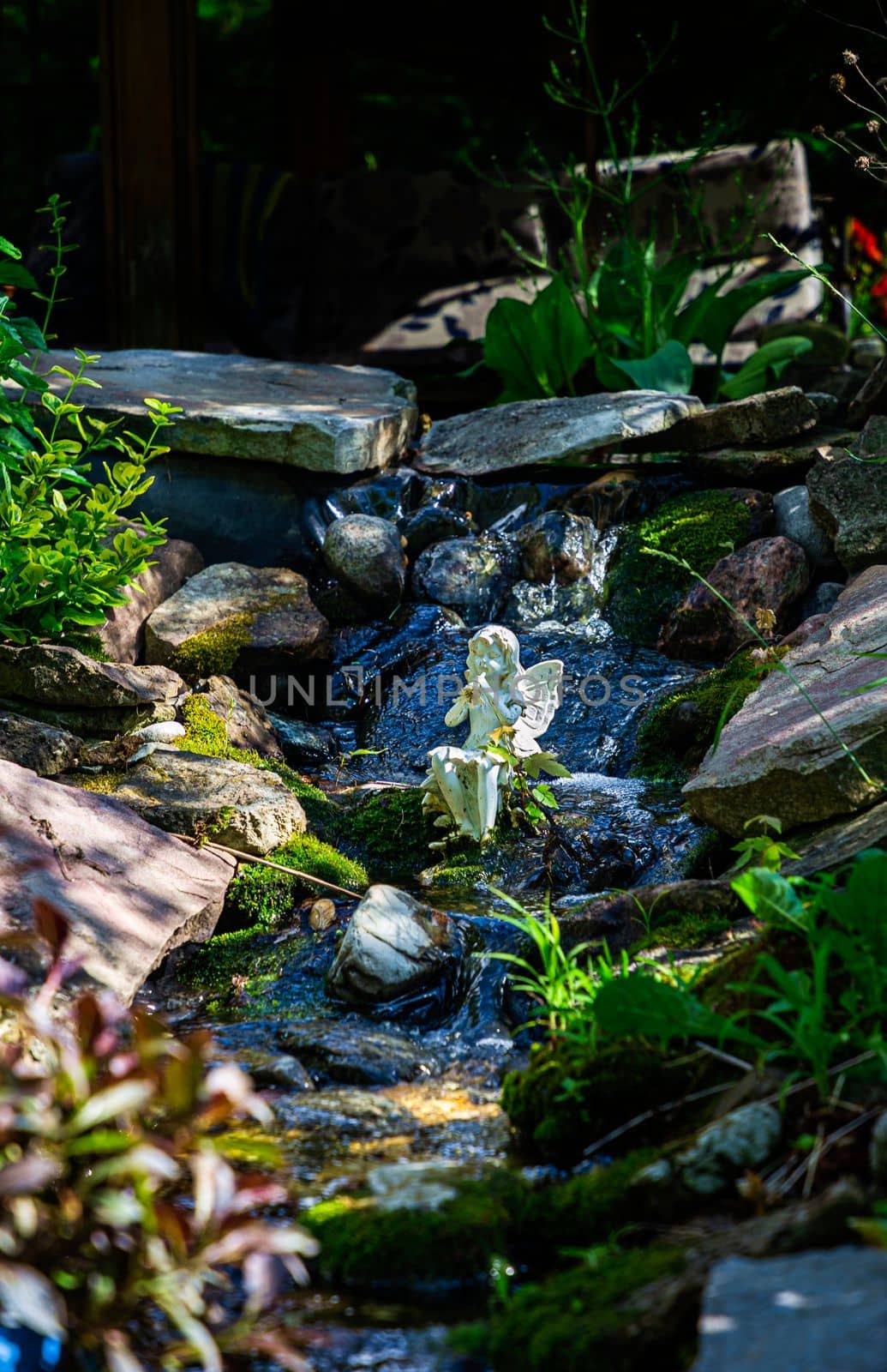 White statue of a faerie playing the flute, sitting in a stream