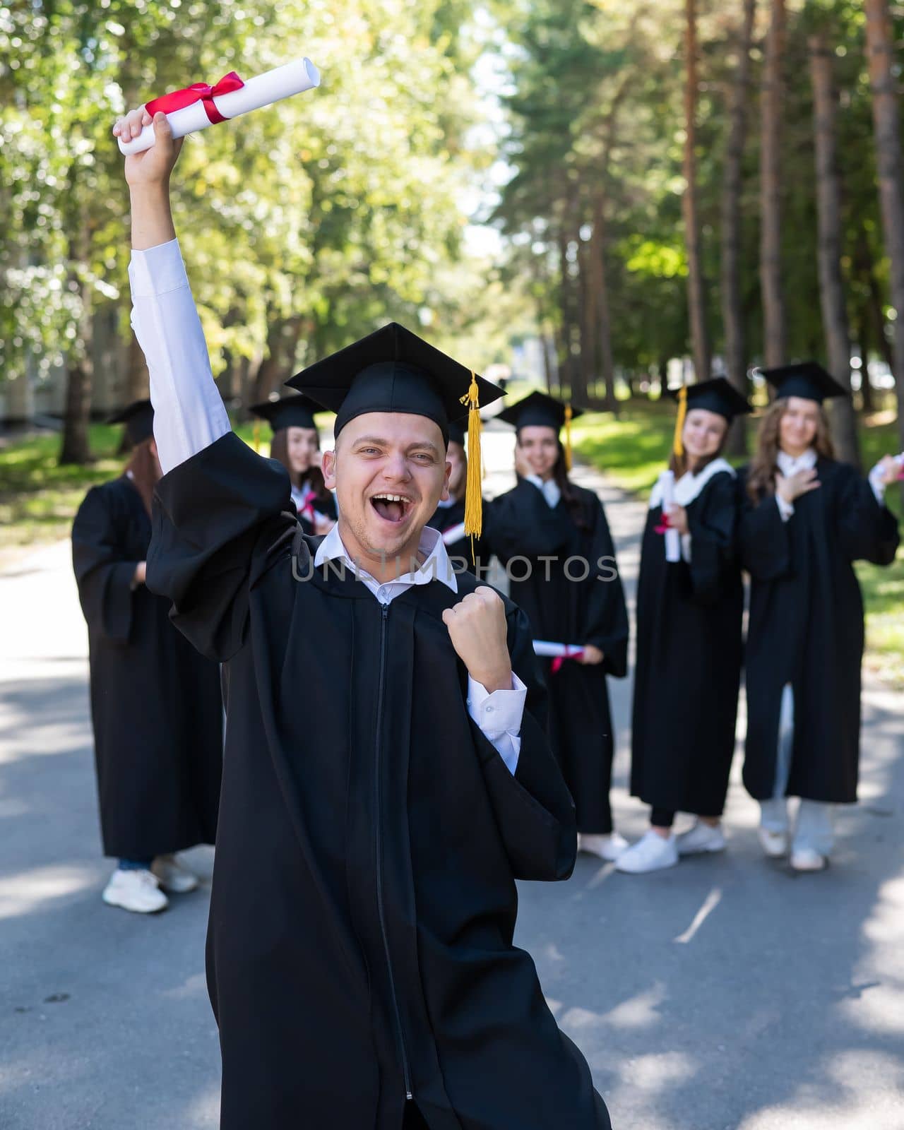 Happy young caucasian man celebrating graduation. Crowd of students graduates outdoors. by mrwed54