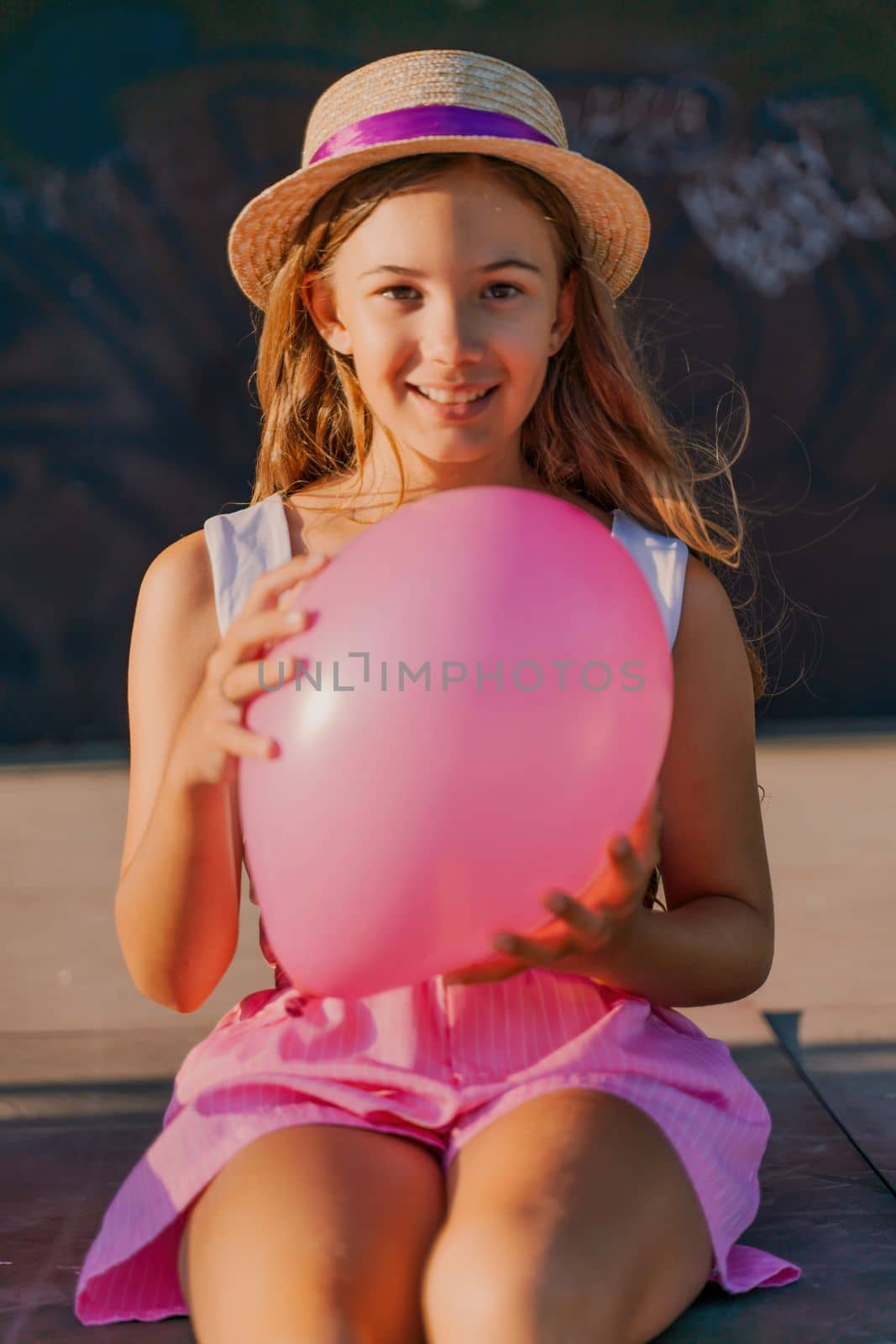 Portrait of a girl in a hat with a pink balloon. She is dressed in pink clothes and her hair is long and loose