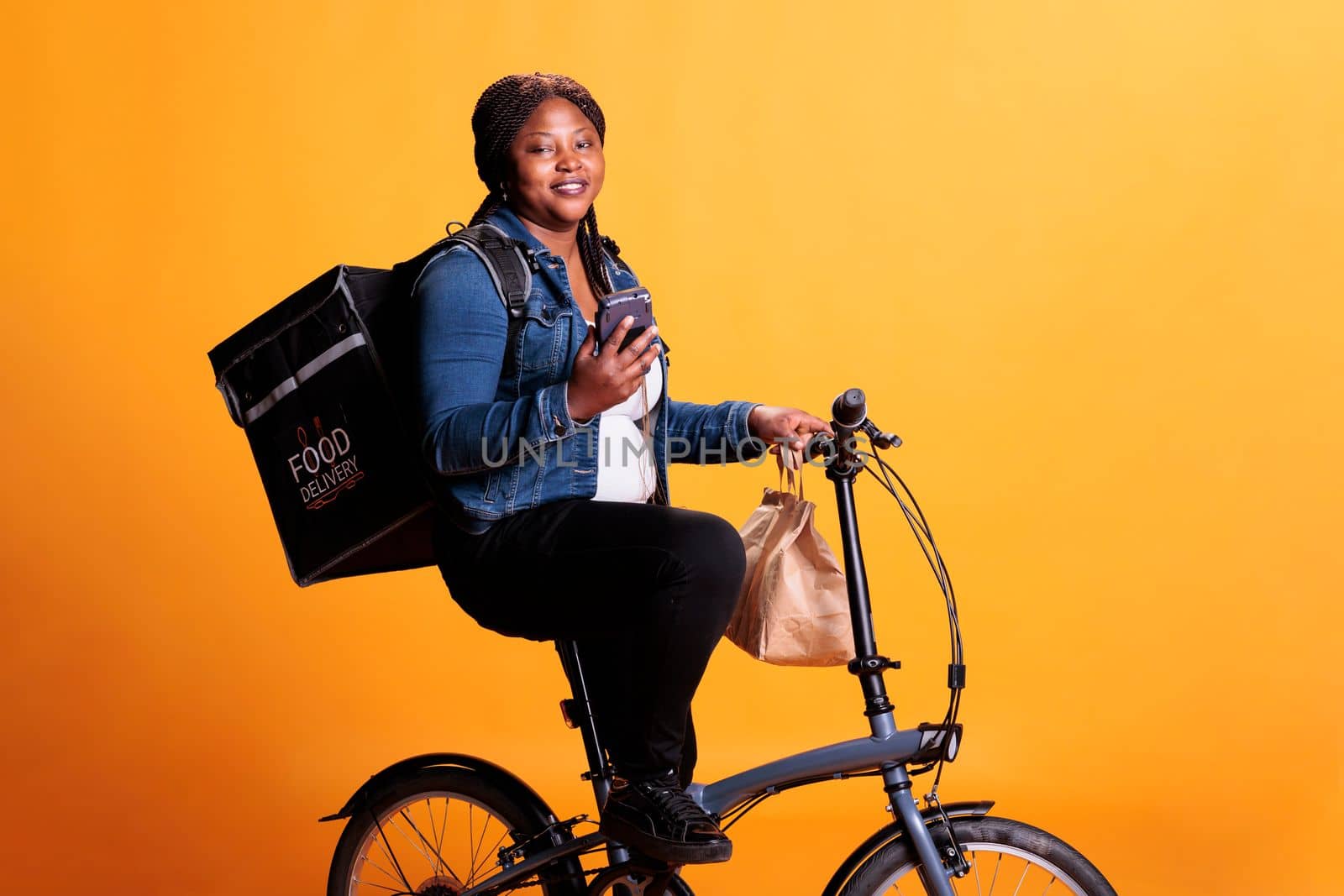 African american restaurant courier looking at client adreess on smartphone before start delivering fast food order to client. Pizzeria employee bringing takeaway meal using bike as transportation